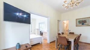 Une chambre avec un lit, une télévision, une table à manger avec des chaises et un lustre.