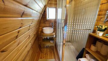 A wooden cabin bathroom with a glass-enclosed shower, a sink, and a shelf with towels.
