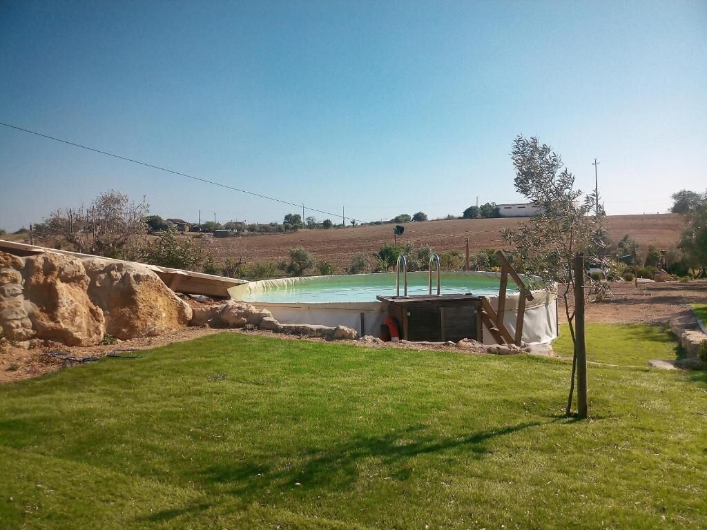 Una piscina con un área verde al frente y un paisaje montañoso en el fondo.