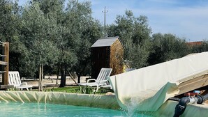 Une piscine avec un toboggan, entourée d’arbres et dotée d’un espace salon extérieur.