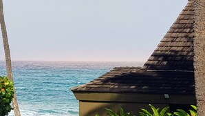 A coastal view with a building featuring a dark roof and a stone wall. - Oceanfront, King Bed, AC, Wi-Fi, Hot Tub, Pool (Lahaina)