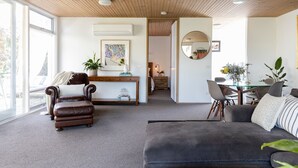 Ein modernes Wohnzimmer mit Ledersessel, grauem Sofa, Holzboden und einem Essbereich mit Glastisch und Stühlen.