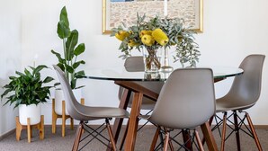 Ein Essbereich mit einem Glastisch, vier Stühlen, einer Blumenvase und einem gerahmten Gemälde an der Wand.