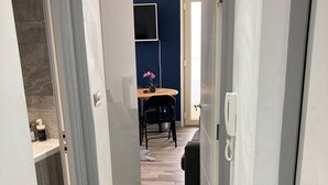 Un pasillo con alfombra oscura que conduce a una habitación con pared azul y una mesa de madera con una silla.