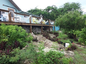 A house with a wooden deck, surrounded by lush greenery and a stone wall. - Historic Island Retreat on Little Exuma (Little Exuma)