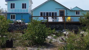 A two-story house with a balcony, surrounded by a garden with various plants and a stone wall. - Historic Island Retreat on Little Exuma (Little Exuma)