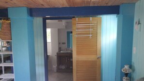 A room with a bed, a wooden door, and a bathroom visible through an open door. - Historic Island Retreat on Little Exuma (Little Exuma)