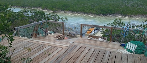 A wooden deck with a hammock and a kayak, overlooking a mangrove-lined waterway.