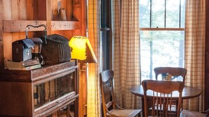 A cozy room with a wooden interior, a table with chairs, a lamp, and a window with curtains. - Signature Cabin 3 with Lake View (Paul Smiths)