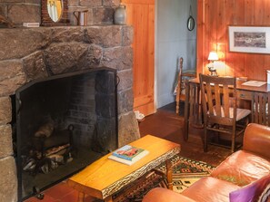 A cozy living room with a stone fireplace, wooden furniture, and a rug. - Signature Cabin 3 with Lake View (Paul Smiths)
