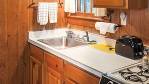 A kitchen with wooden cabinets, a stainless steel sink, a toaster, and a gas stove. - Signature Cabin 3 with Lake View (Paul Smiths)