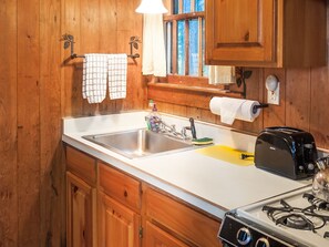 A kitchen with wooden cabinets, a stainless steel sink, a toaster, and a gas stove. - Signature Cabin 3 with Lake View (Paul Smiths)