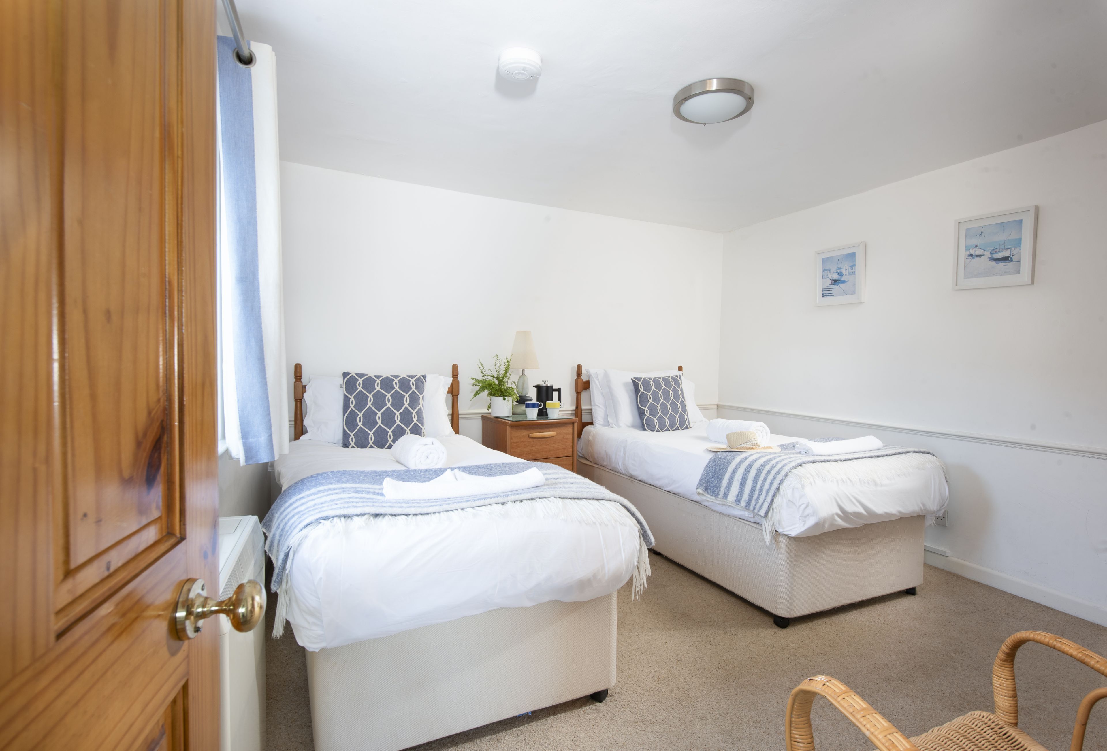 A bedroom with two beds, a wooden door, a nightstand with a lamp, and a small table.