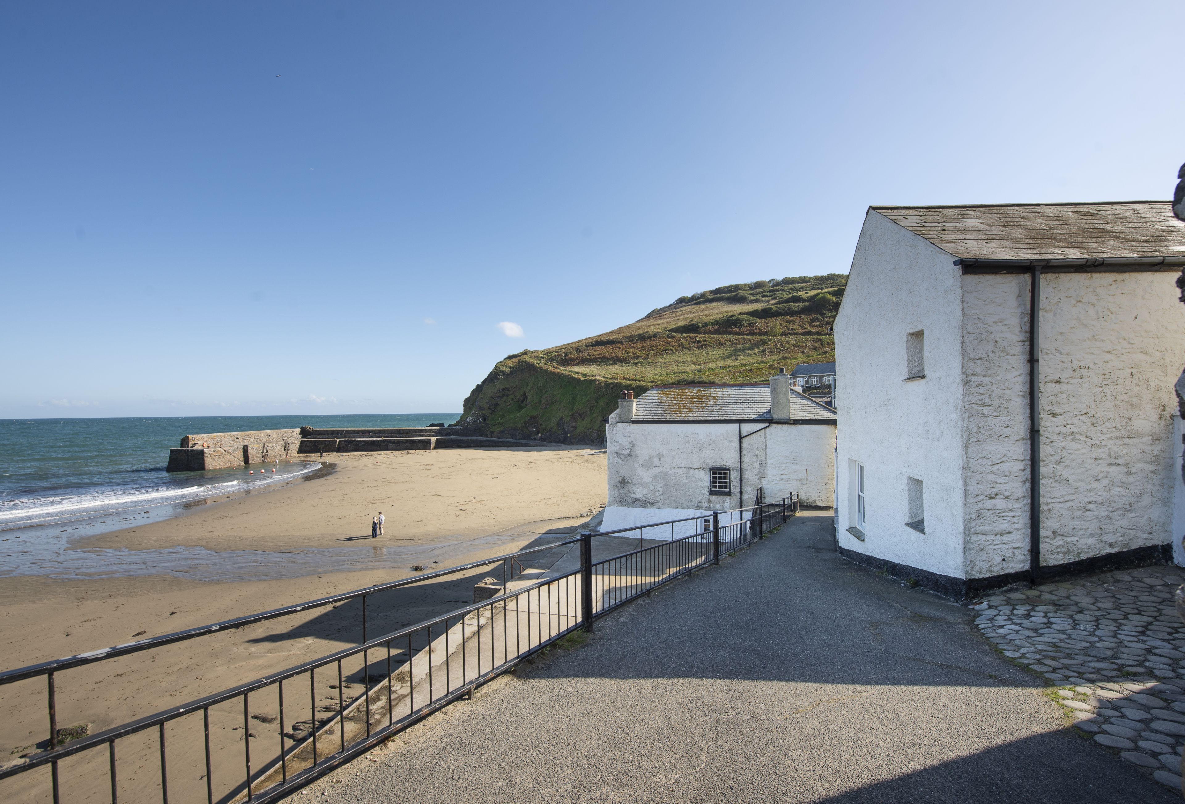 A coastal building with a paved walkway leading to a sandy beach.