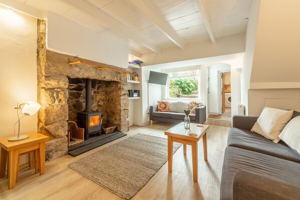A cozy living room with a stone fireplace, wooden furniture, and a view of the outdoors.