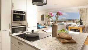A modern kitchen with built-in ovens, a stove, and a dining area with a view. - A stunning, environmentally friendly holiday haven at Mor Cliff, in an AONB. (Chapel Porth)