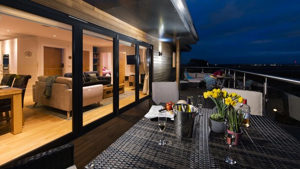 A modern outdoor living area with a dining table set for two, a comfortable seating area, and a view of the ocean. - A stunning, environmentally friendly holiday haven at Mor Cliff, in an AONB. (Chapel Porth)
