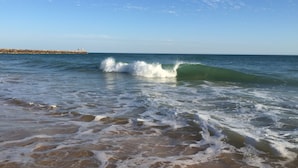 A beach with waves and a rocky outcrop in the distance. - CASA JOY Vilamoura Apartment (Vilamoura)