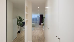 A modern hallway with wooden flooring, white walls, and a glass door leading to a room with a view. - CASA JOY Vilamoura Apartment (Vilamoura)