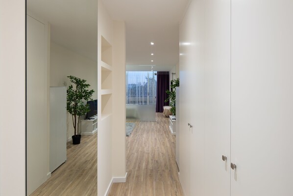 A modern hallway with wooden flooring, white walls, and a glass door leading to a room with a view. - CASA JOY Vilamoura Apartment (Vilamoura)