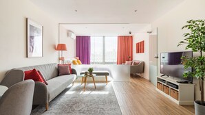 A modern living room with a grey sofa, a small round table, and a TV stand with a flat-screen TV. - CASA JOY Vilamoura Apartment (Vilamoura)