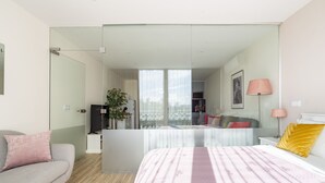 A modern bedroom with a bed, a sofa, a desk, and a large window. - CASA JOY Vilamoura Apartment (Vilamoura)