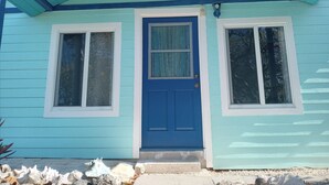 Ein kleines Haus mit blauer Tür und zwei Fenstern, einer Veranda mit Stufen und einem hellblauen Anstrich.