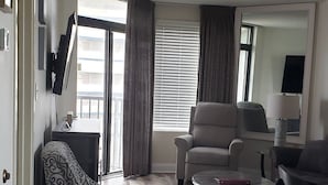 A living room with a patterned armchair, a sofa, a coffee table, and a TV mounted on the wall. - Beautifully Updated Condo in Beachfront Resort.   (Myrtle Beach)