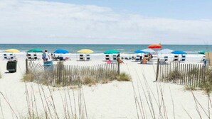 A beach with rows of beach chairs and umbrellas, a wooden fence, and the ocean in the background. - Beautifully Updated Condo in Beachfront Resort.   (Myrtle Beach)