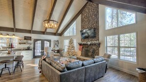 A spacious living area with a fireplace, a large sofa, and a kitchen area with bar stools. - #AzStoneCabin- Finest Luxury Cabin In Pinetop- Lakeside! (Pinetop)