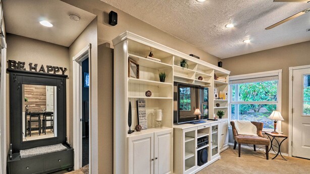 A living room with a built-in entertainment unit, a seating area with a chair, and a window with a view of greenery. - Cute & Cozy PDX Area Townhouse: 31 Mi to Mt. Hood! (Boring)