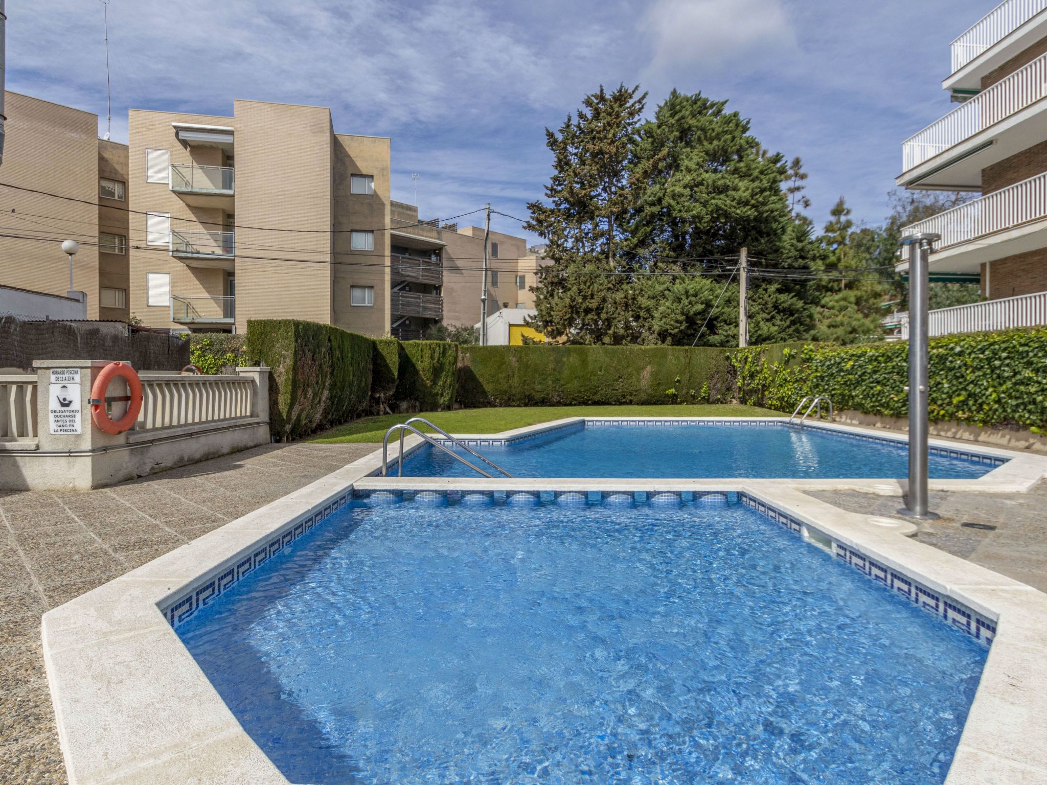 A swimming pool area with two pools, surrounded by apartment buildings and greenery.
