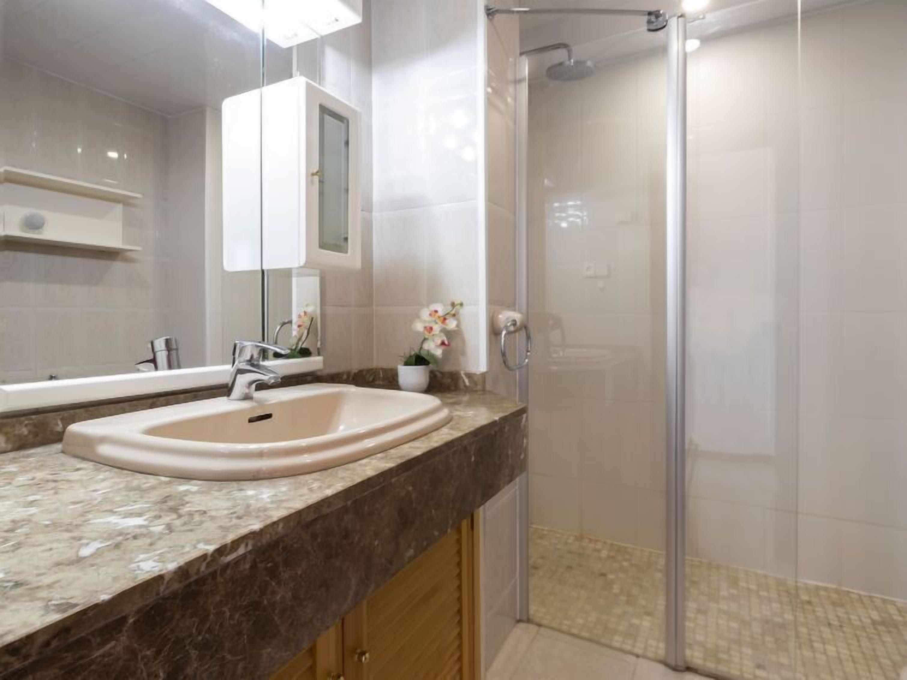 A bathroom with a marble countertop, a sink, a mirror, and a glass-enclosed shower.