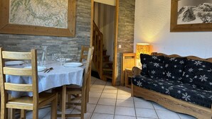 A dining area with a table set for four, wooden chairs, a stone wall, and a sofa with a patterned cover.