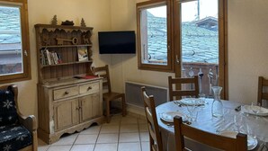 A dining area with a wooden cabinet, a TV mounted on the wall, and a window with a view of a building.