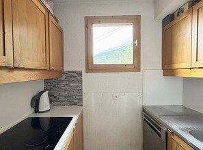 A compact kitchen with wooden cabinets, a stone backsplash, a window with a view, and a dishwasher. - Le Bourg-Morel 1 - Charming duplex apartment in the village centre (LES AVANCHERS VALMOREL)