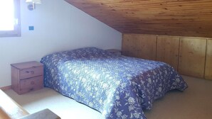 A bedroom with a sloped ceiling, wooden walls, a bed with a floral bedspread, a nightstand, and a wall-mounted lamp. - Le Mucillon 39 - 2-room apartment, close to the ski slopes, facing south (LES AVANCHERS VALMOREL)