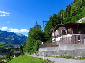 A mountain village with a wooden house featuring a balcony and a concrete wall.
