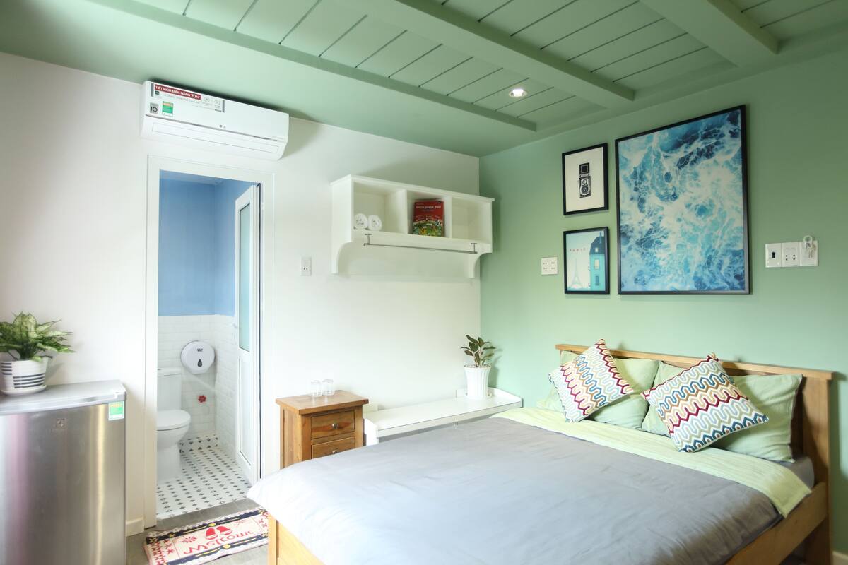A bedroom with a bed, a bedside table, a small bedside table, a wall-mounted shelf, a wall-mounted air conditioner, a wall-mounted light switch, a wall-mounted electrical outlet, a wall-mounted picture frame, and a wall-mounted picture frame.