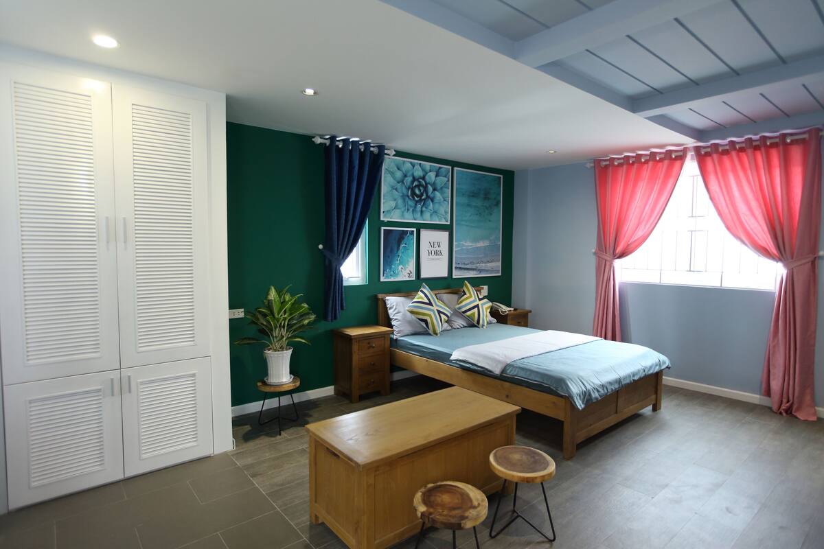A bedroom with a bed, bedside tables, a wooden bench, a potted plant, and a wardrobe.