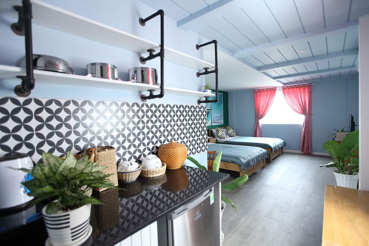 A modern kitchen with a black countertop, white and black patterned backsplash, and a stainless steel refrigerator. There are shelves above the counter holding pots and a potted plant.