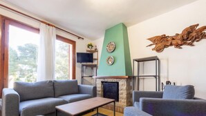 Una sala de estar con chimenea, sofás grises, una mesa de centro y un televisor sobre un mueble.