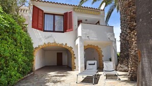 Una villa con un patio de piedra, dos sillones y un pequeño arco que conduce a una zona cubierta.