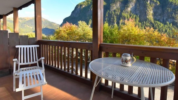Un balcon avec une chaise et une table blanches, donnant sur un paysage montagneux aux couleurs automnales.
