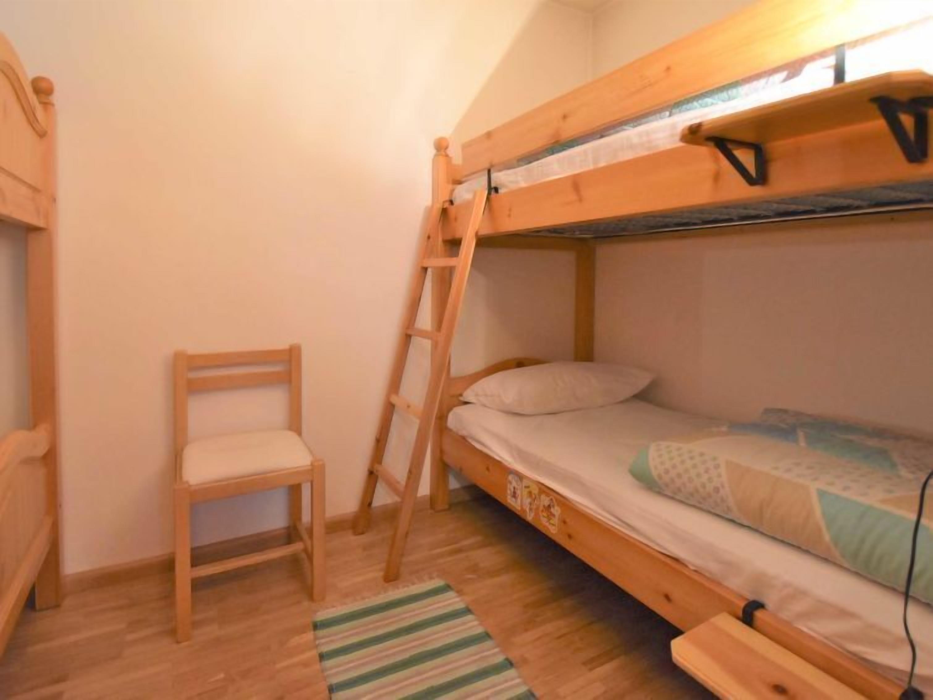 Una stanza con un letto a castello, una scala in legno, una sedia e un tappeto a righe.