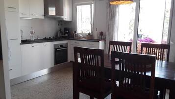 Een koelkast, een oven, kookgerei, borden en bestek, een eettafel