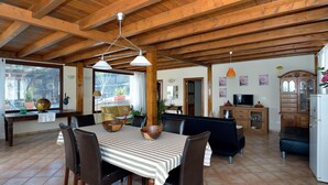 Un vaste espace de vie doté d’un plafond en bois, d’une table à manger avec des chaises, d’un canapé, d’un téléviseur et d’un meuble de rangement.