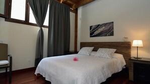 Une chambre à coucher bien rangée, avec un lit, une lampe de chevet, une petite table et une fenêtre avec des rideaux.