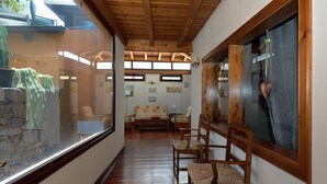 Un couloir doté d’un plancher en bois, d’un mur en pierre et d’une porte en verre donnant sur une pièce où se trouvent un canapé et des fauteuils.