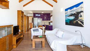 Un vaste espace de vie doté d’un plafond en bois, d’un canapé blanc, d’une table basse en bois et d’un téléviseur posé sur un meuble en bois.